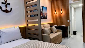 A hotel room with a bed, a desk, a sofa, and a wall-mounted picture.