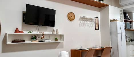 Habitación de hotel con cama, televisor, escritorio con silla, reloj y estante con adornos.