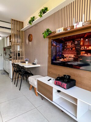 A modern living space with a dining area, a TV mounted on a wooden wall, and a Netflix logo on a white table. - Mahrak Villa - VSH (Ipojuca)
