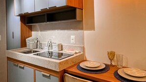 A compact kitchen with a sink, stove, and cabinets, a dining table with chairs, and a hanging light fixture. - Mahrak Villa - VSH (Ipojuca)
