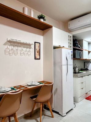 A modern kitchen with a dining area, white cabinetry, a refrigerator, a microwave, and a small plant on the shelf.