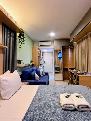 A hotel room with a bed, a seating area with a sofa, a desk, a television, and a wardrobe. - Mahrak Villa - VSH (Ipojuca)