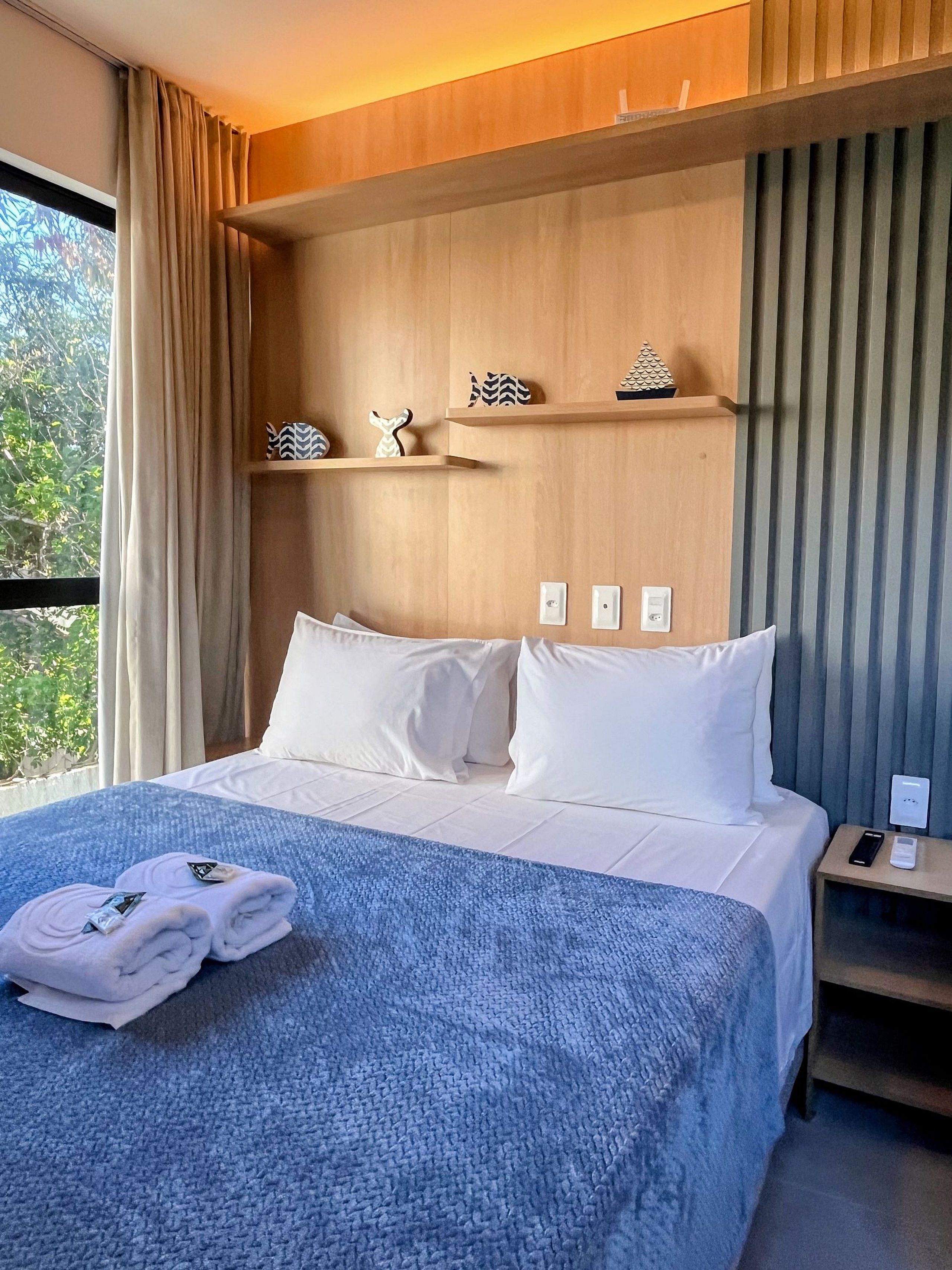 Una habitación de hotel con una cama, una mesita de noche y un ventanal con cortinas.