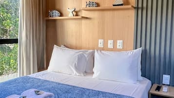 Una habitación de hotel con una cama, una mesita de noche y un ventanal con cortinas.