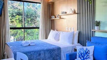 A hotel room with a bed, a blue sofa, a dining table with plates and a cup, and a window with curtains.