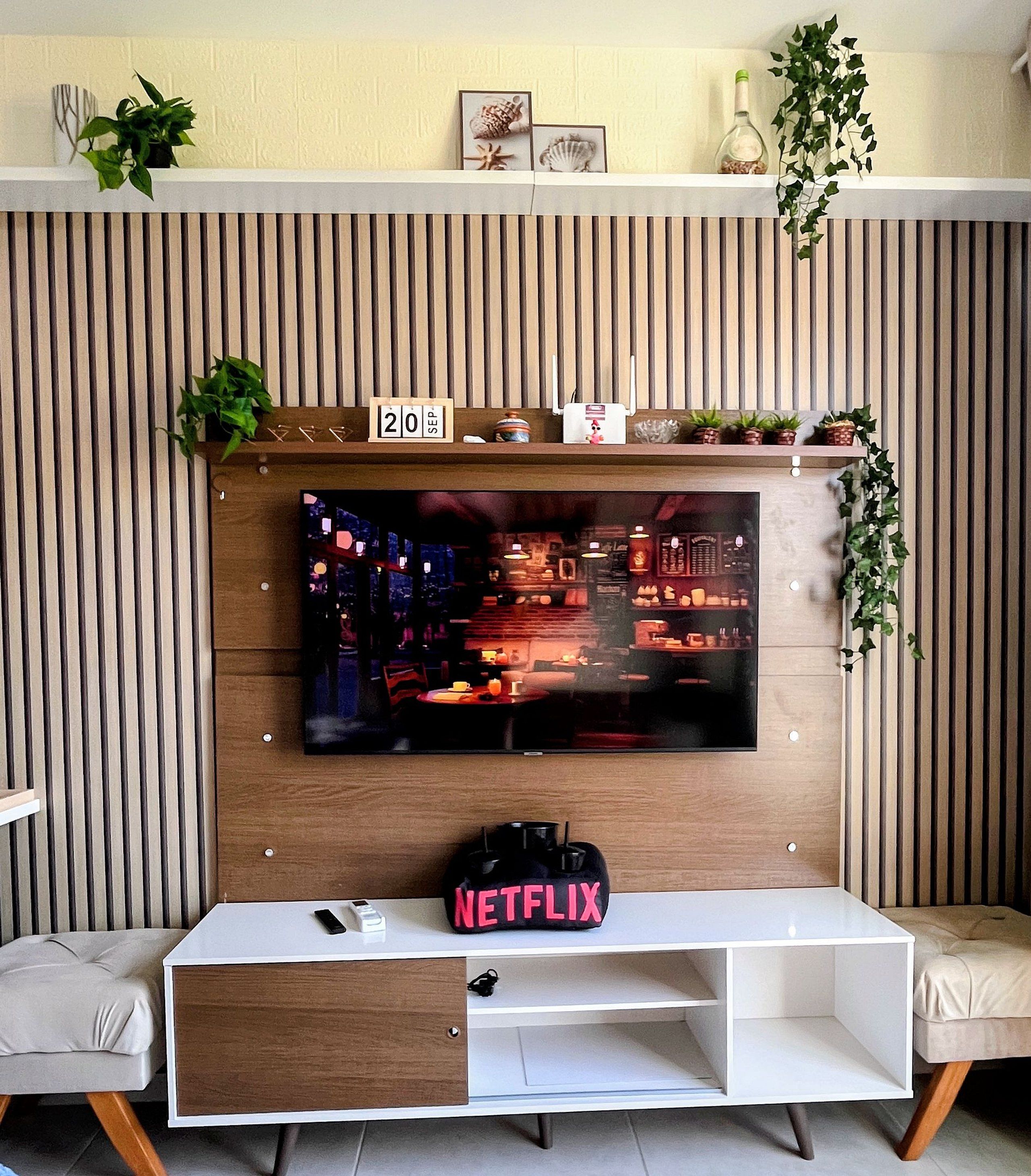 A modern living room with a flat-screen TV mounted on a wooden wall, a white entertainment unit below, and a date display above the TV.