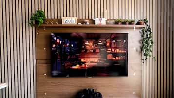 A modern living room with a flat-screen TV mounted on a wooden wall, a white entertainment unit below, and a date display above the TV.