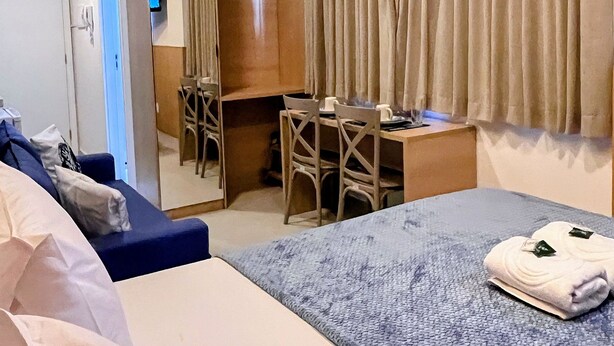 A hotel room with a bed, a desk, a chair, a wardrobe, and an air conditioning unit. - Mahrak Villa - VSH (Ipojuca)