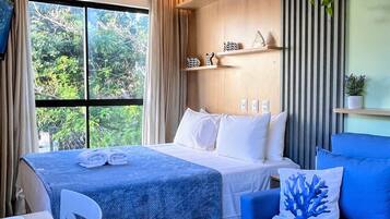 Una habitación de hotel con cama, un sofá azul, una mesa de comedor con platos y una taza, y una ventana con cortinas.