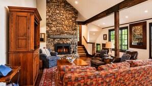 A cozy living room with a stone fireplace, wooden furniture, and a staircase leading to another level. - Hawk’s Landing | Hot Tub, Views & Game Room (Banner Elk)