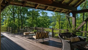 Una terraza de madera con mobiliario exterior, una pérgola y vistas a un área boscosa.