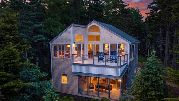 Une cabane à deux étages avec un balcon, entourée d’arbres.