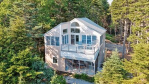 Une maison à deux étages dotée d’un balcon, entourée d’une forêt dense.
