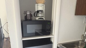 A compact kitchen with a black microwave, a coffee maker, and a stainless steel refrigerator.