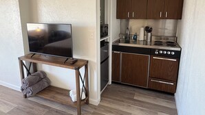 A compact kitchen with wooden cabinets, a stove, and a sink. A flat-screen TV is placed on a wooden table with towels.