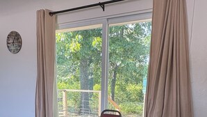 A room with a round wooden table, two red chairs, a window with curtains, and a clock on the wall.