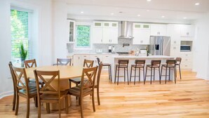 Una cucina moderna con mobili bianchi, un'isola centrale con sgabelli da bar e un'area pranzo con sedie in legno.