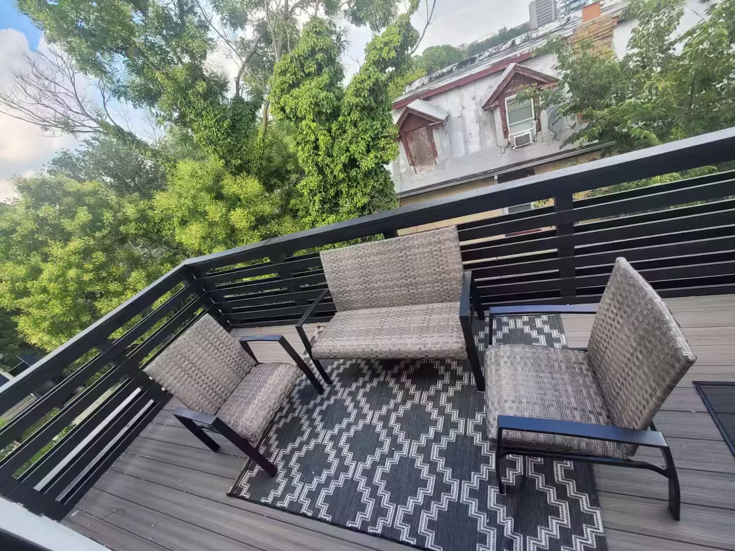 A deck with wicker furniture and a patterned rug, surrounded by a wooden deck and metal railing.