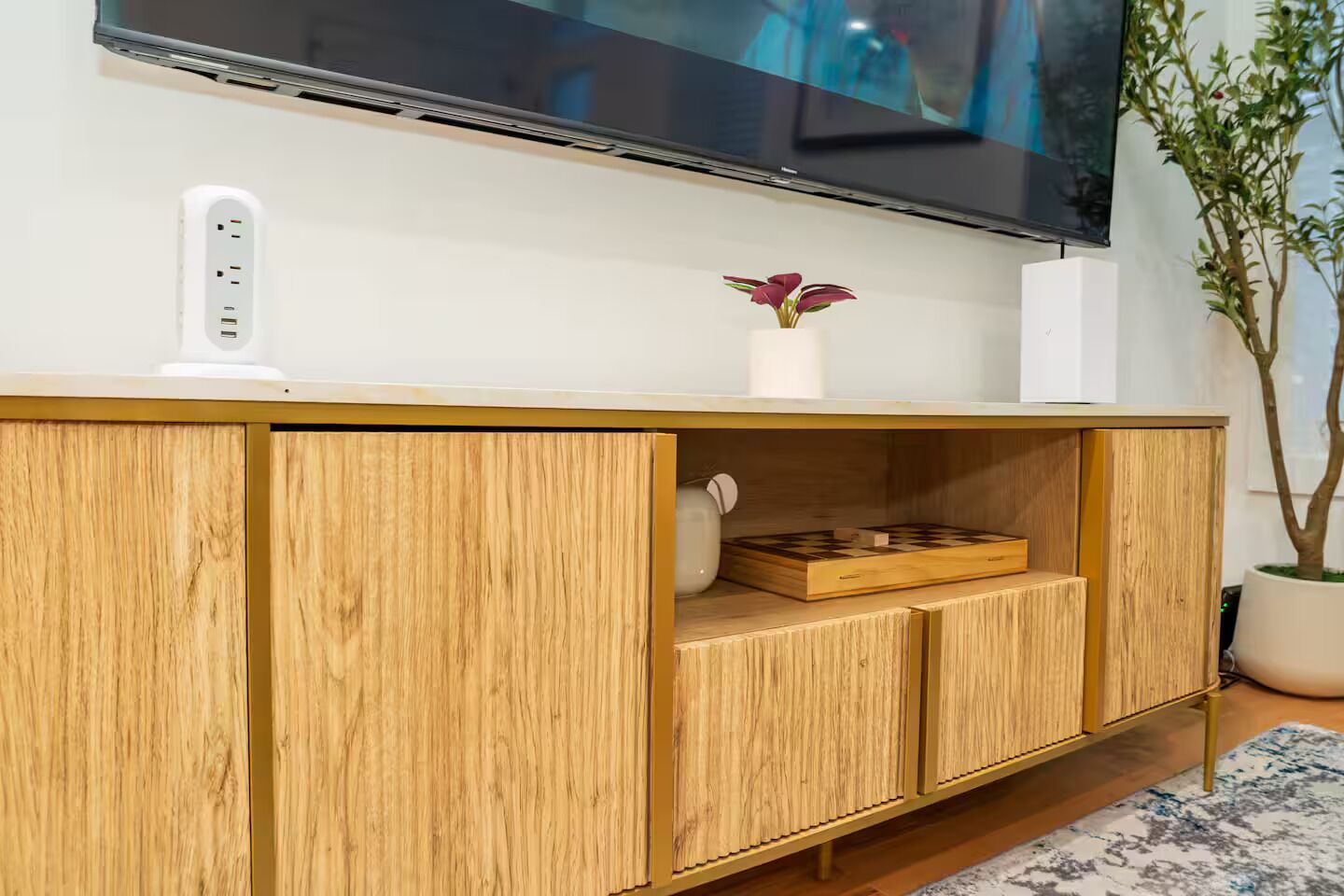 Ein Holz-Fernsehschrank mit einem flachbildfernseher darüber, einer Steckleiste, einer Vase mit Blumen und einem Schachbrett.