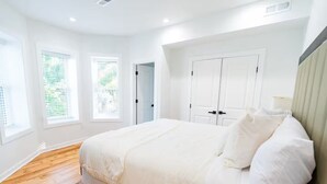 Une chambre avec un grand lit, des murs blancs et un plancher en bois.