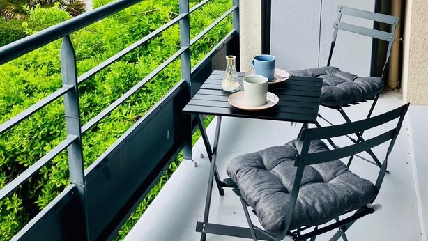 Ein Balkon mit Tisch und Stühlen, einer Tür und Blick auf Grünflächen und Gebäude.