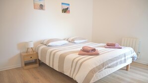 Ein ordentlich bezogenes Bett mit gestreifter Bettwäsche und zwei Kissen, ein Nachttisch mit Lampe und ein Heizkörper an der Wand.