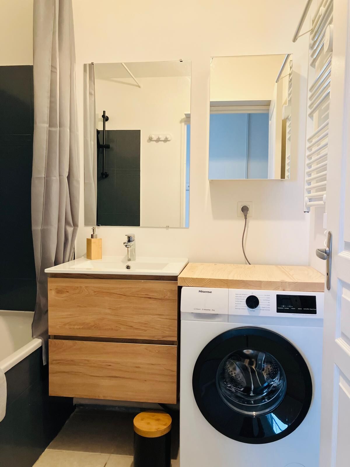 A modern bathroom with a wooden vanity, a washing machine, and a mirror.