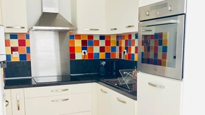 Eine moderne Küche mit weißen Schränken, einer schwarzen Arbeitsplatte, einer farbenfrohen Spritzschutzwand und einer Edelstahl-Dunstabzugshaube.