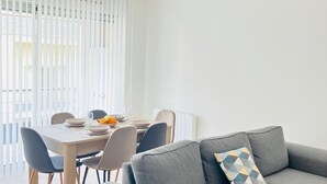 Ein modernes Wohnzimmer mit einem grauen Sofa, einem Esstisch gedeckt mit Tellern und Gläsern, und einer Deckenleuchte.
