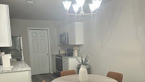 A modern kitchen with white cabinets, a built-in oven, and a microwave. There is a dining area with a round table and four chairs.