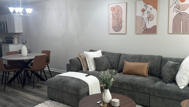 A modern living room with a grey sectional sofa, a round coffee table, and a dining area with a chandelier.