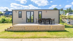 A single-story wooden cabin with a deck, two sliding glass doors, and a small patio area with a table and chairs.