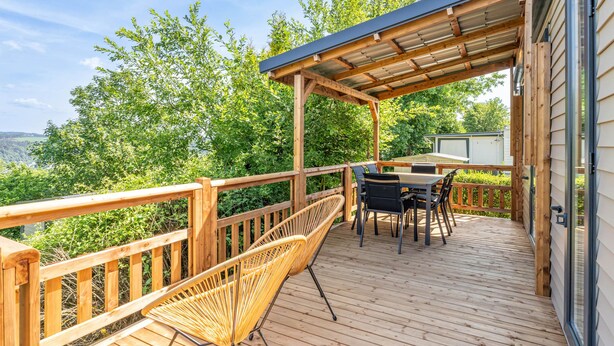 A wooden deck with a covered seating area, a table, and chairs.