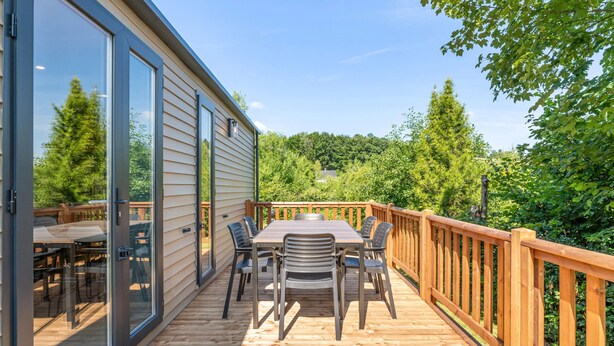 Une terrasse dotée d’une table et de chaises, entourée d’une rambarde en bois, et offrant une vue sur une zone boisée.