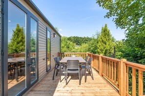 A deck with a table and chairs, a wooden railing, and a glass door leading to an outdoor area.