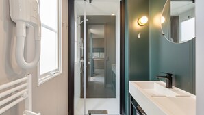 A modern bathroom with a walk-in shower, a white sink, and a hairdryer mounted on the wall.