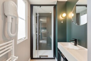 A modern bathroom with a walk-in shower, a white sink, and a hairdryer mounted on the wall.