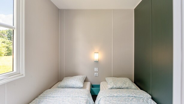 A room with two beds, a window, a wall-mounted light, and a green accent wall.