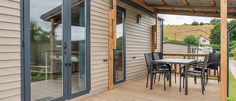 Una terraza con mesa y sillas, una puerta corrediza de vidrio y una estructura de pérgola.
