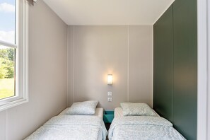 A room with two beds, a window, a wall-mounted light, and a green accent wall.