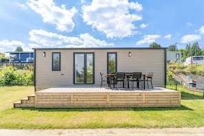 A single-story wooden cabin with a deck, two sliding glass doors, and a small patio area with a table and chairs.