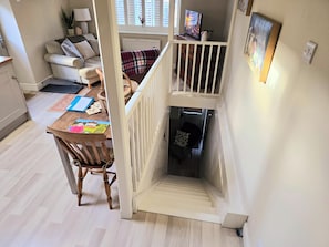 Eine Treppe führt zu einer unteren Ebene, einem Essbereich mit Tisch und Stühlen sowie einem Wohnzimmer mit Sofa und Fernseher.