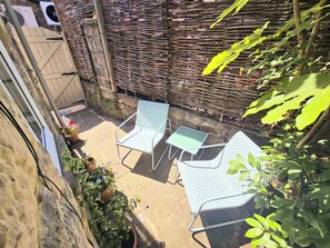 Eine Terrasse mit zwei Metallstühlen, einem Tisch, einer Steinmauer und einem Geflechtzaun.