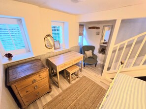 Ein Zimmer mit einem hölzernen Schminktisch, einem Schreibtisch, einem Stuhl, einem Fenster mit Jalousien und einer Treppe.
