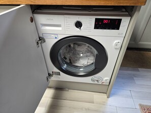 En tvättmaskin med frontmatning, en digital display, en kontrollpanel med olika inställningar och en etikett som anger en garanti på tre år.