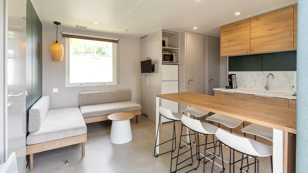 A modern kitchen with a wooden countertop, white bar stools, and a built-in microwave. - Camping Papillon Bouillon - Maison Chachelle (Bouillon)