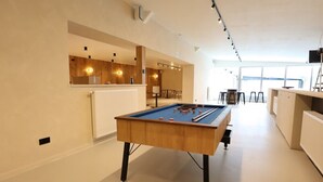 A pool table in a room with a kitchen area and a view to the outside.