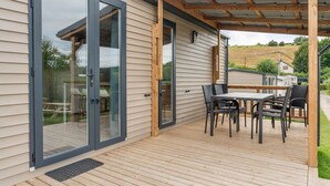 A deck with a table and chairs, a sliding glass door, and a pergola structure. - Camping Papillon Bouillon - Maison Chachelle (Bouillon)