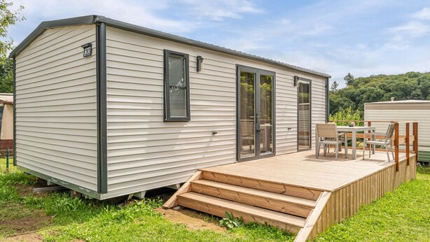 Una casa móvil con terraza, puerta corredera y una pequeña mesa y sillas al aire libre.