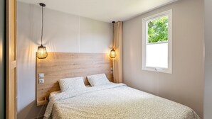 Un dormitorio con cabecera de madera, dos lámparas de noche, una ventana con vistas a zonas verdes y una cama con ropa de cama estampada.